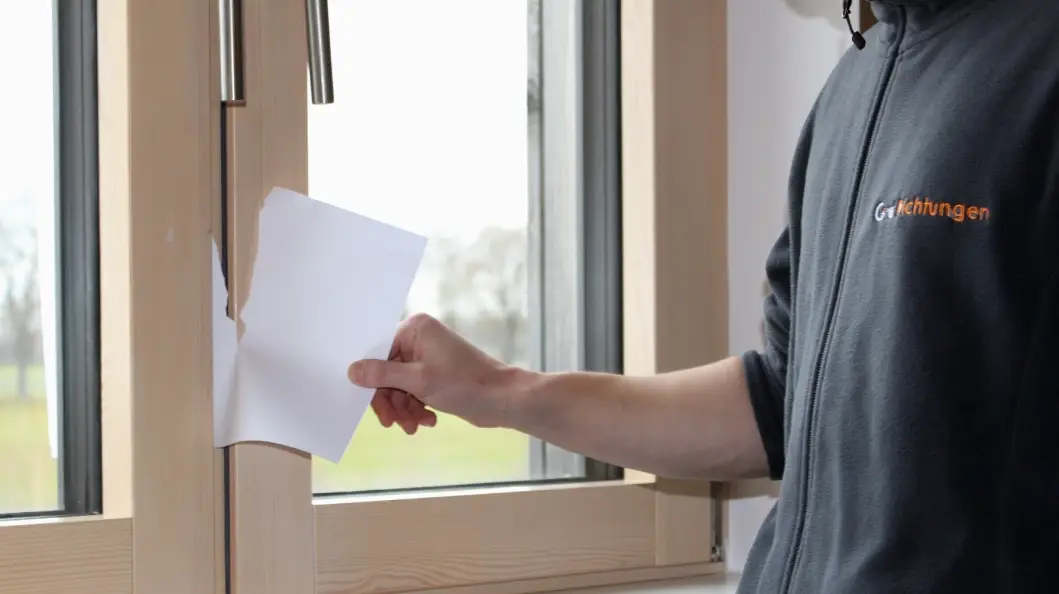 Mann prüft auf  Zugluft durch die Fensterdichtung mit einem Papier