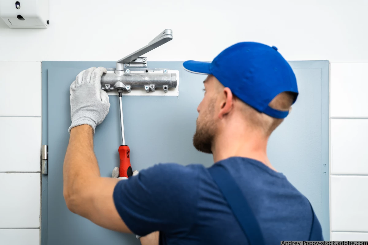 Handwerker montiert Tuerschliesser an die Tuer