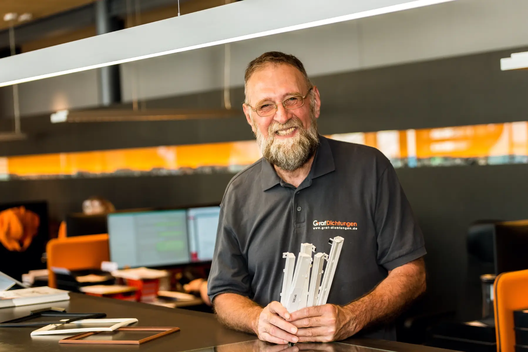 Dichtung-Sonderanfertigung-Experte-Graf-Dichtungen lächelnder Mitarbeiter hält ein Bündel Fensterfalzlüfter in den Händen