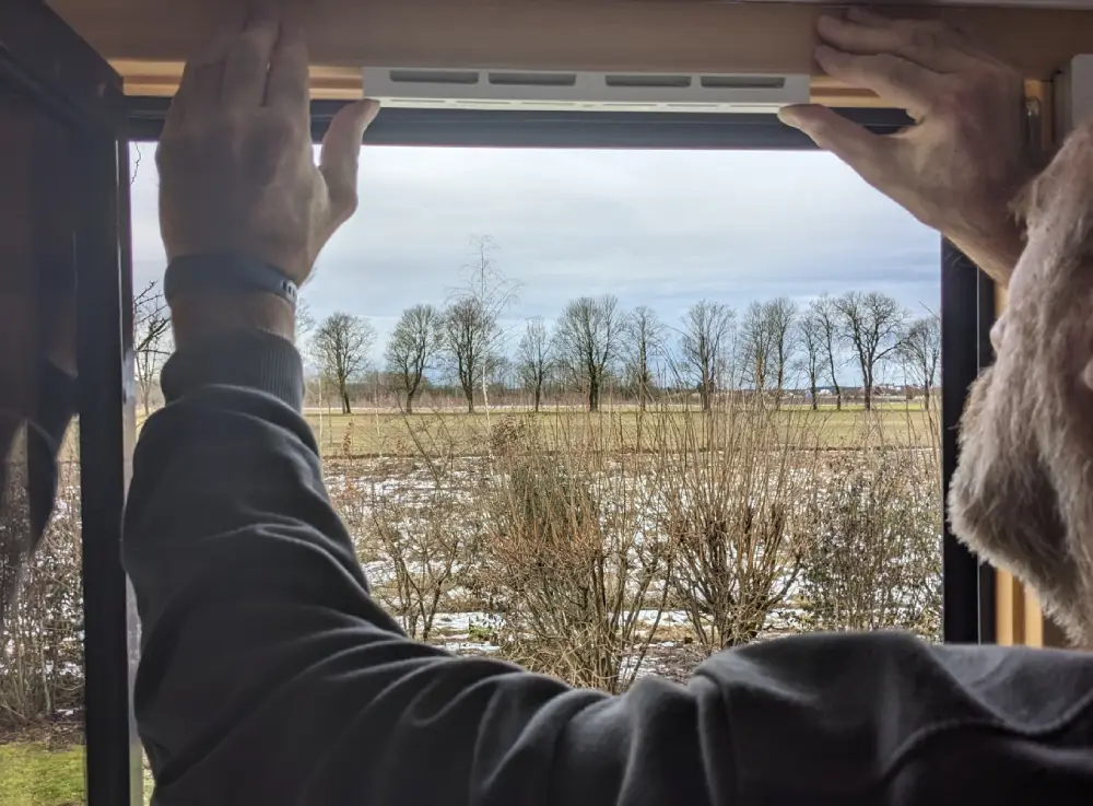 Person baut Fensterfalzlüfter an den Fensterrahmen